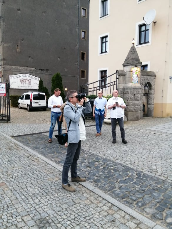 Zdjęcie kilku osób stojących a na pierwszym planie mężczyzna robiący zdjęcia