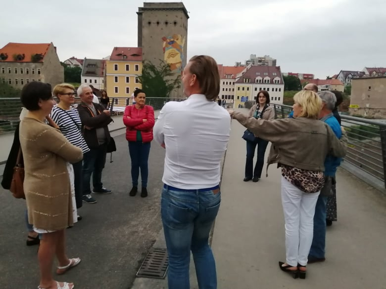 Stojąca grupa osób na moście i słuchająca przewodnika, w tle stare miasto